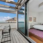 Schlafzimmer mit Blick auf Terrasse und Wasser. Holzboden, Bett, Kunst an der Wand.