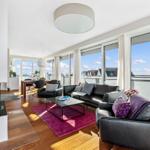 Wohnbereich mit Kamin, Ledersofa und großem Fensterblick auf Wasser.