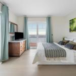 Schlafzimmer mit Bett, Fernseher und Blick aufs Meer.