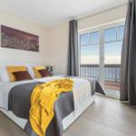 Schlafzimmer mit Blick auf die See, Bett mit Kissen und Decke, Fenster zur Terrasse.