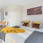 Schlafzimmer mit Bett, Wandbild und Nachttischen. Holzfußboden und Spiegel.