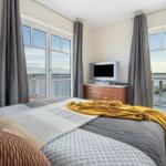 Schlafzimmer mit Blick auf Wasser und Balkon. Bett mit Decke, Fernseher und Schrank.
