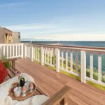 Terrasse mit Blick auf das Meer, Holzbank, Kissen, Tisch mit Frühstück.
