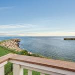 Blick von Balkon auf Meer mit Steinhafeneinfassung und grüner Fläche