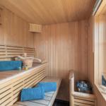 Sauna mit Holzbank, blauen Handtüchern und Blick auf Außenbereich.