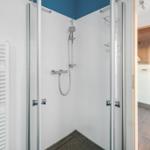 Dusche mit Glaswand und Heizkörper. Sauna im Hintergrund.