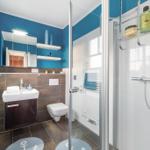Badezimmer mit Dusche, Waschbecken und Toilette. Blaue Wände und runde Teppiche mit Ankern.