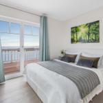 Schlafzimmer mit Blick aufs Meer und Balkon. Bett, Nachttische und Fernseher.