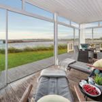 Terrasse mit Loungemöbeln und Blick auf Wasser und Grasfläche.