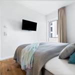 Schlafzimmer mit Bett, Fernseher und Fenster mit Blick auf Gebäude.