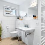 Badezimmer mit Toilette, Waschbecken und Heizkörper. Fenster, Pflanze und Spiegel sichtbar.