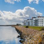 Wohnhaus am Wasser mit Steinufer und blauem Himmel mit Wolken.