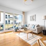 Wohnzimmer mit Sofa, Kamin und Terrasse. Holzboden und große Fenster.