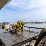 Terrasse mit Tisch, Stühlen und Blick auf Wasser und Gebäude