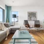 Wohnzimmer mit Sofa, zwei Sesseln, Tisch und Blick auf Balkon.