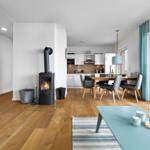 Wohnzimmer mit Kamin, Essbereich und Küche. Holzboden und große Fenster.