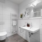 Badezimmer mit Toilette, Waschbecken und Heizkörper. Weiße Fliesen und Spiegel.
