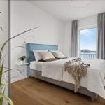 Schlafzimmer mit Bett, Fensterblick auf Wasser und Stuhl.