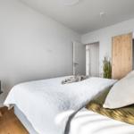 Schlafzimmer mit Bett, Stuhl und Spiegel. Holzboden und weiße Wände.