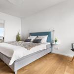 Schlafzimmer mit Bett, Stuhl und Spiegelschrank. Holzboden und blaues Kopfteil.