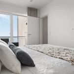 Schlafzimmer mit Balkon und Blick auf Meer. Bett mit Kissen und Decke.