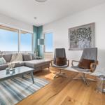 Wohnzimmer mit Sofa, zwei Sesseln, Couchtisch und Blick auf Balkon.