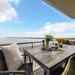 Terrasse mit Tisch, Stühlen und Meerblick. Blumen und Früchte auf dem Tisch.