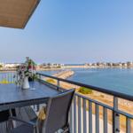 Terrasse mit Tisch und Stühlen, Blick auf Hafen und Küste.