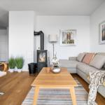 Wohnzimmer mit Sofa, Kaminofen und Holztisch. Küche im Hintergrund.