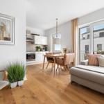 Wohnbereich mit Essbereich und Küche. Holzboden, Sofa, Essgruppe und Fenster zum Balkon.
