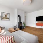 Wohnzimmer mit Sofa, Kaminofen, Fernseher und Holzboden.