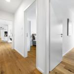 Flur mit Holzboden, Blick in Küche, Schlafzimmer und Wohnbereich mit Balkon.