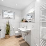 Badezimmer mit Toilette, Waschbecken und Heizung. Fenster mit Pflanze und Spiegel.