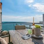 Terrasse mit Tisch, Stühlen und Meerblick. Tisch mit Geschirr und Pflanze.