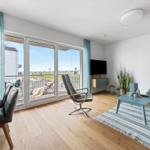Wohnbereich mit Balkon, Sofa, Sessel und TV. Holzboden und blaue Akzente.