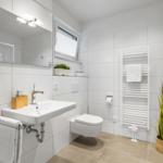 Badezimmer mit Waschbecken, Spiegel, Toilette und Heizung. Pflanze und Handtuchhalter sichtbar.