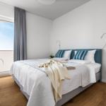 Schlafzimmer mit Doppelbett, Fenster und Pflanze.