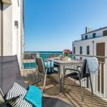 Terrace with table, chairs, and sea view. Blue cushions and flowers on the table.