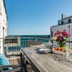 Terrace with table, chairs, and sea view. Flowers and fruit on the table.