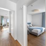 Bedroom with bed and view into living area with dining space and balcony.