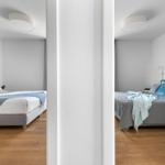 Two bedrooms with beds, blankets, and chairs. Wooden floor and white walls.
