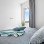 Bedroom with bed, pillows, and view of outside through window.