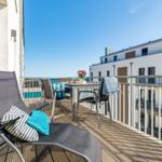 Balcony with lounge chair, table, and chairs. View of buildings and sea.