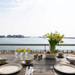 Gedeckter Tisch mit Meerblick, Blumen und Obst auf Balkon.