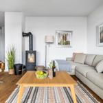 Wohnzimmer mit Sofa, Kamin und Holztisch. Küche im Hintergrund.