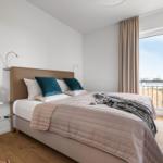 Schlafzimmer mit Bett, Fenster und Pflanzen. Holzboden und Wandhalterungen.