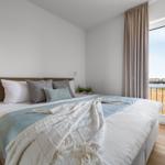 Schlafzimmer mit Blick auf Wasser, großes Bett mit Kissen und Decke, Holzboden und Fenster.