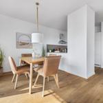 Essbereich mit Holztisch, braunen Stühlen und Küchenbereich im Hintergrund.