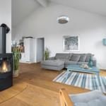 Wohnzimmer mit Kamin, Sofa und Holzboden. Küche im Hintergrund.