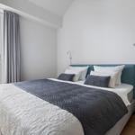 Schlafzimmer mit Bett, Fenster und Balkon. Wandlampen und graue Vorhänge.